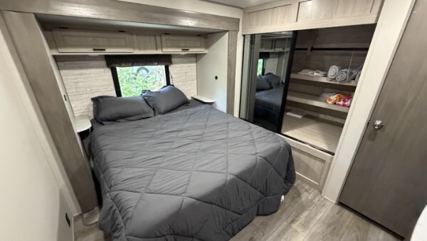 Comfortable RV bedroom with a queen bed, overhead storage, and mirrored wardrobe