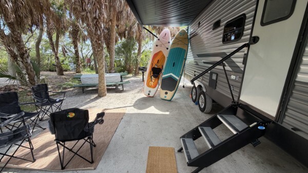 RV campsite with outdoor chairs, paddleboards, and a shaded camping area