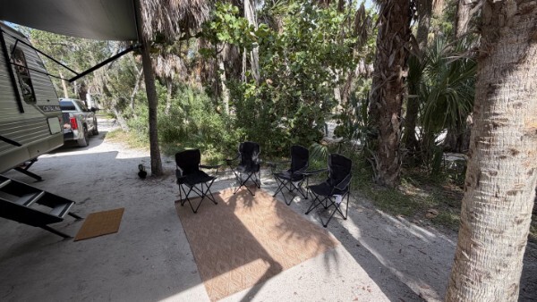 RV campsite with outdoor chairs, paddleboards, and a shaded camping area