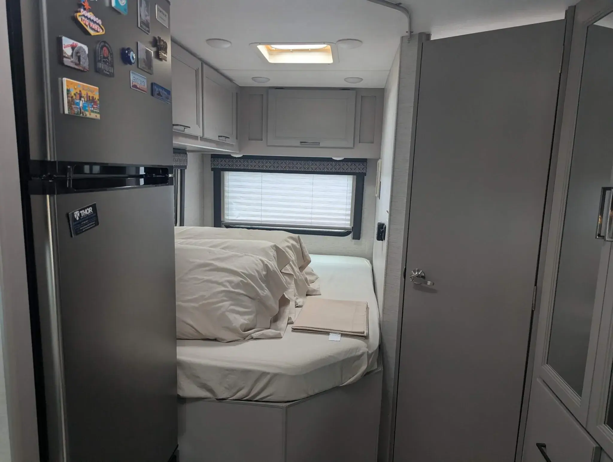 Small motorhome bedroom with bed, window, and overhead storage